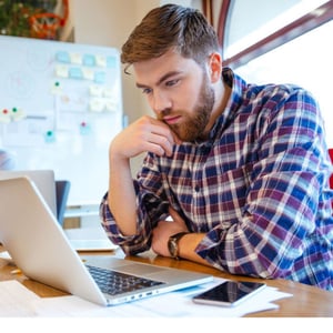 Concentrated bearded young man using laptop while his friends studying together